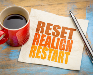 Photograph of a coffee cup sitting on top of a white napkin that reads: "reset, realign, restart" in an orange font.