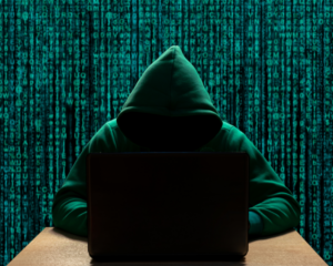 Hooded man sitting on a laptop on front of green binary code